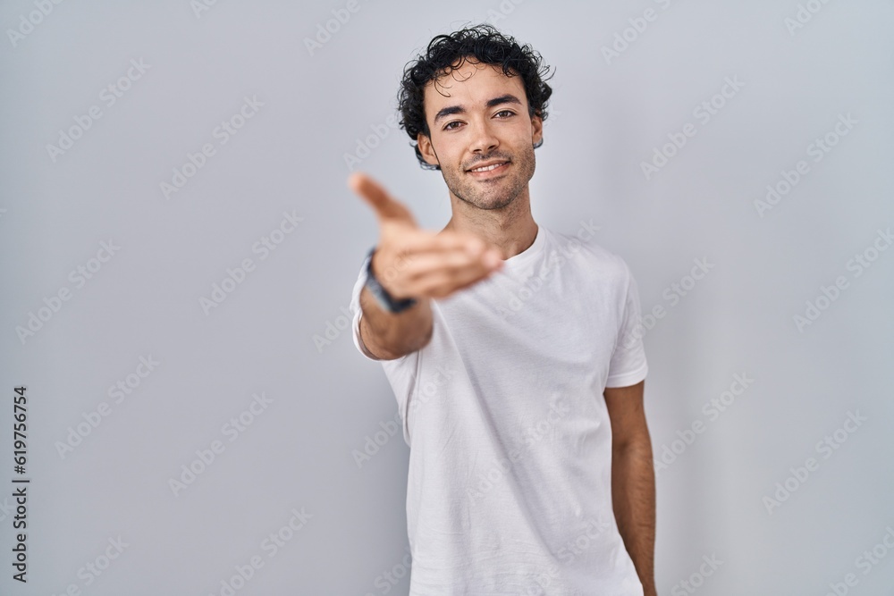 Hispanic man standing over isolated background smiling friendly offering handshake as greeting and welcoming. successful business. Hispanic man standing over isolated background smiling friendly offering handshake as greeting and welcoming. successful business.