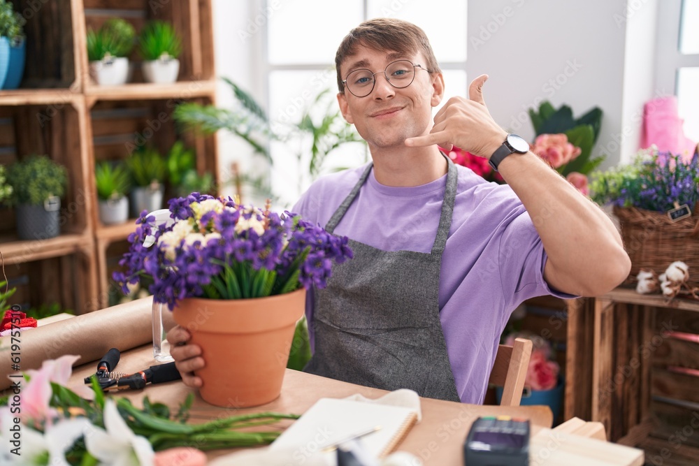 Caucasian blond man working at florist shop smiling doing phone gesture with hand and fingers like talking on the telephone. communicating concepts.