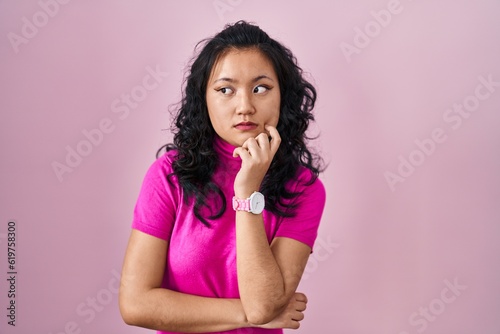 Young asian woman standing over pink background looking stressed and nervous with hands on mouth biting nails. anxiety problem.