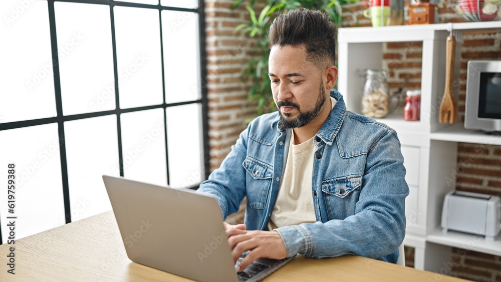 Young latin man using laptop sitting on table at dinning room Young latin man using laptop sitting on table at dinning room