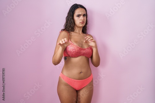 Young hispanic woman wearing lingerie over pink background disgusted expression, displeased and fearful doing disgust face because aversion reaction.