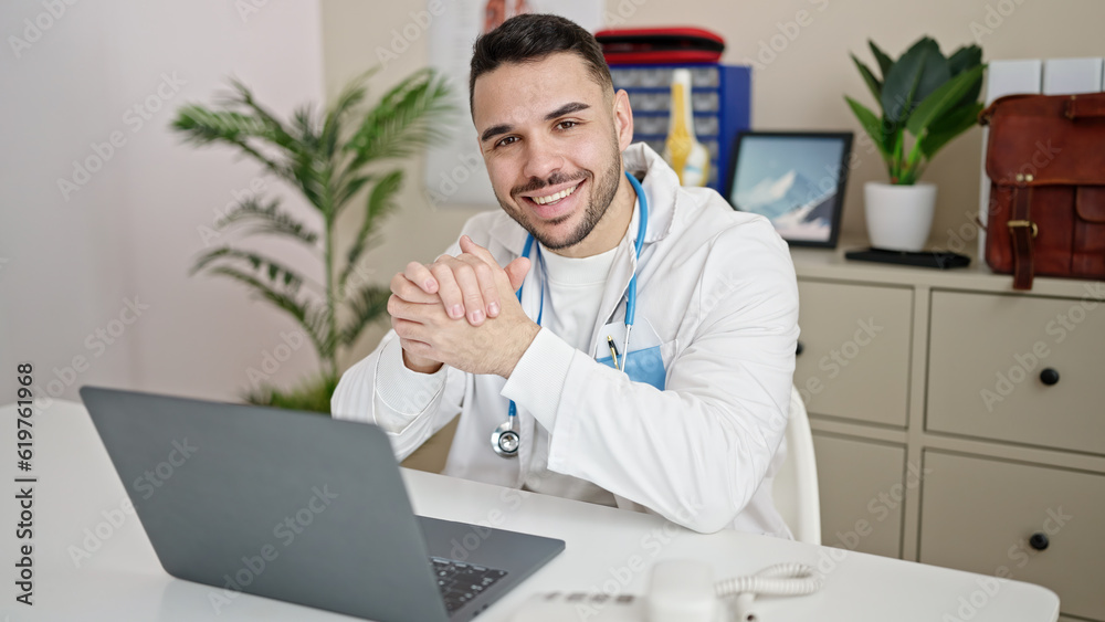 Young hispanic man doctor using laptop working at clinic