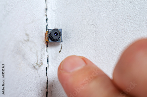Spy hidden camera in the crack of the wall. Man discovers micro camera in office. Spy scandal, collecting compromising evidence, wiretapping, symbolic image. photo