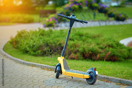 Electric scooter for rent stand on parking zone in city park. Yellow electric scooter parked in the city, rent service. E-scooter sharing for walking around. Selective focus