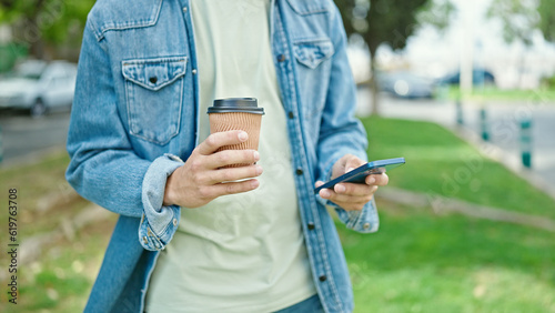Young caucasian man using smartphone drinking coffee at park