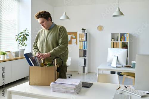 Obraz na plátne Young office worker standing at his workplace and packing his things in box afte
