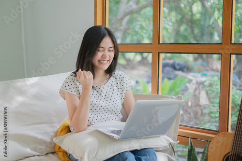 Attractive Asian female is enjoy working at home office. Concept of rejoice, success, celebrate. Win a lottery or gambling. Finished work. Job complete. Achievement of project. Cheerful expression.