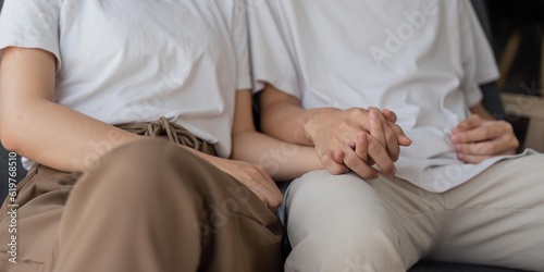 hands closeup of an adult romantic couple sitting on a couch in home interior © Natee Meepian