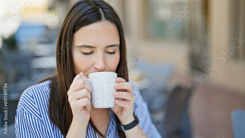 Young beautiful hispanic woman drinking coffee sitting on table at coffee shop terrace
