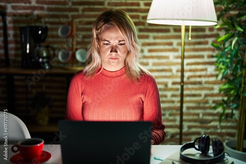 Blonde woman using laptop at night at home skeptic and nervous, frowning upset because of problem. negative person.