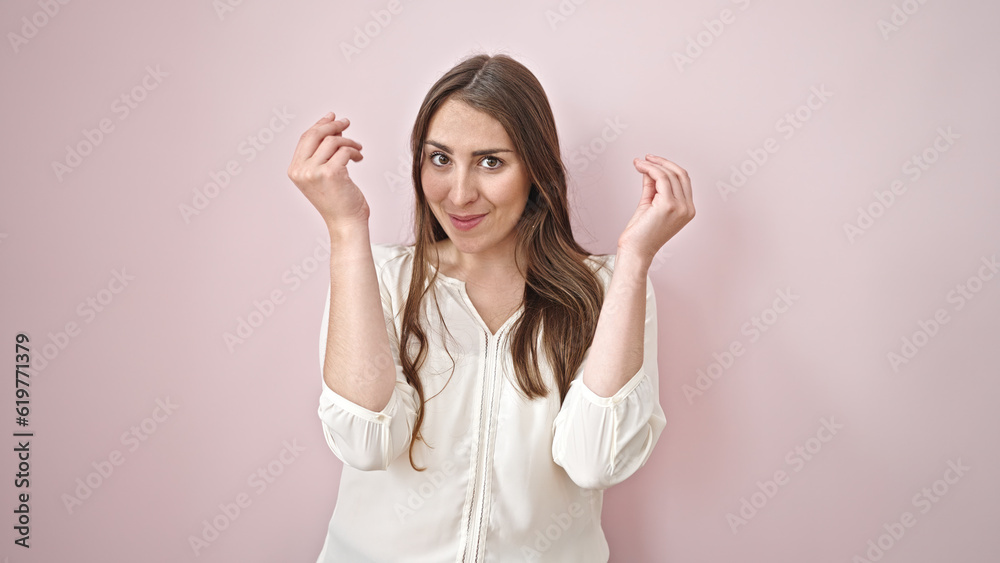 Young beautiful hispanic woman smiling confident doing money gesture over isolated pink background Young beautiful hispanic woman smiling confident doing money gesture over isolated pink background