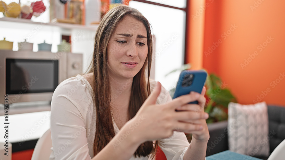 Young beautiful hispanic woman using smartphone looking upset at dinning room Young beautiful hispanic woman using smartphone looking upset at dinning room