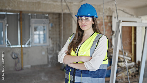 Young beautiful hispanic woman builder standing with arms crossed gesture and relaxed expression at construction site