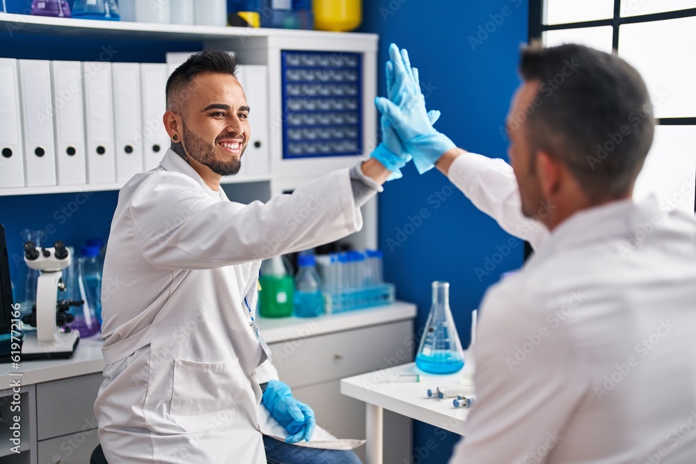 Two men scientists smiling confident high five with hands raised up at laboratory