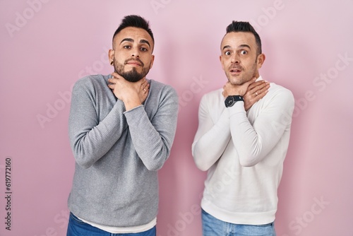 Homosexual couple standing over pink background shouting suffocate because painful strangle. health problem. asphyxiate and suicide concept.