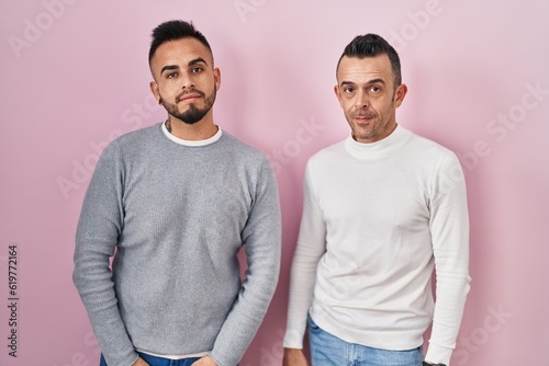 Homosexual couple standing over pink background relaxed with serious expression on face. simple and natural looking at the camera.