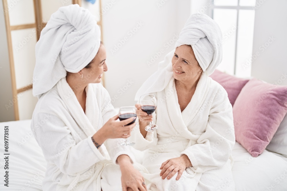 Mother and daughter wearing bathrobe drinking glass of wine at bedroom