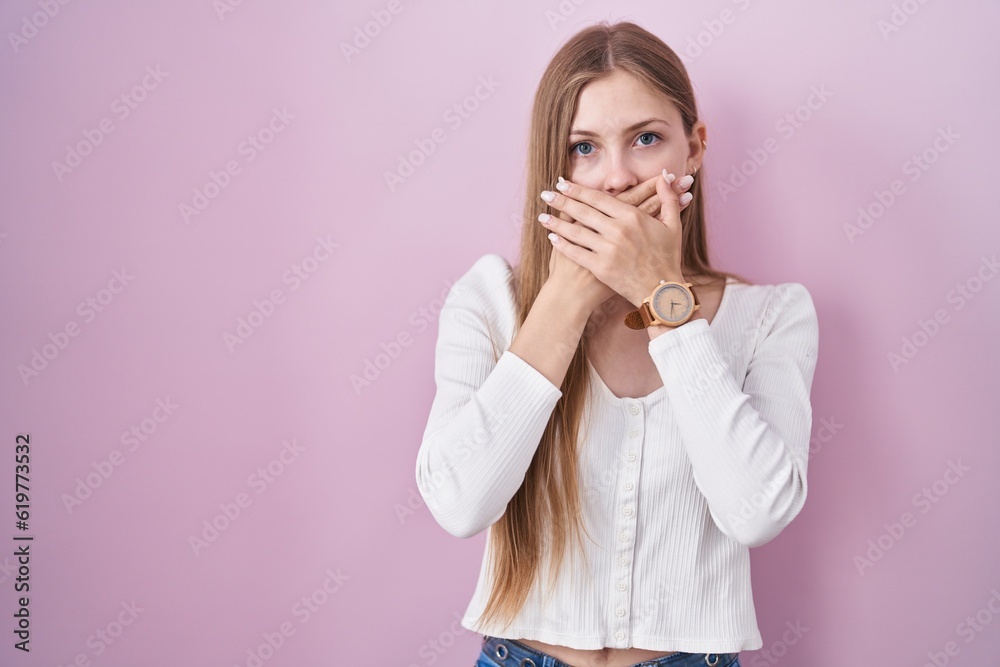 Young caucasian woman standing over pink background shocked covering mouth with hands for mistake. secret concept. Young caucasian woman standing over pink background shocked covering mouth with hands for mistake. secret concept.