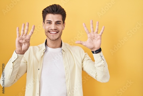 Young hispanic man standing over yellow background showing and pointing up with fingers number nine while smiling confident and happy. © Krakenimages.com