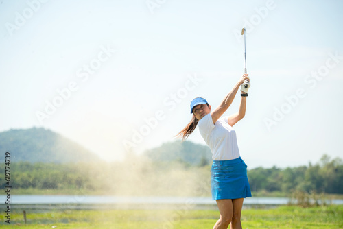 Golfer sport course golf ball fairway. People lifestyle woman playing game golf and hitting go on green grass river and mountain background.  Asia female player game shot in summer.