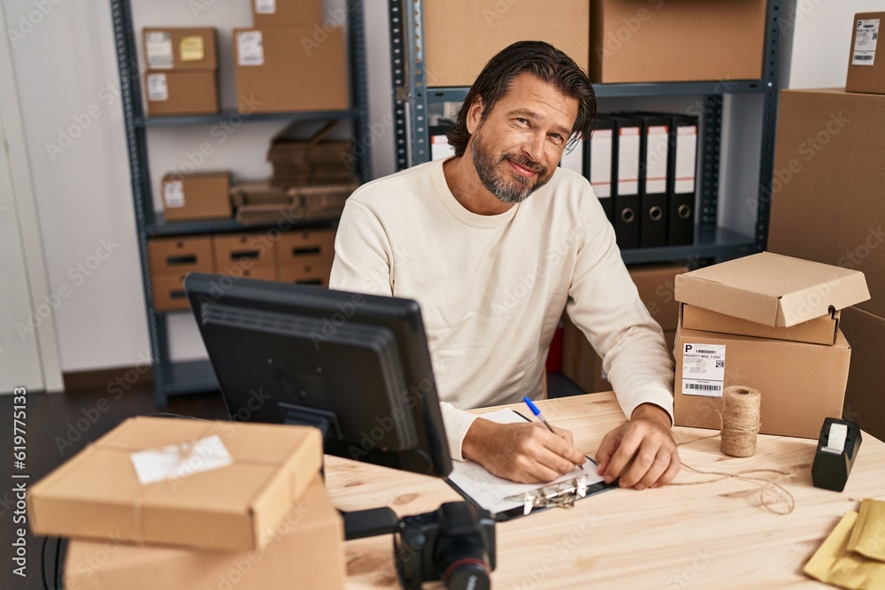 Middle age man ecommerce business worker using laptop writing on document at office Middle age man ecommerce business worker using laptop writing on document at office