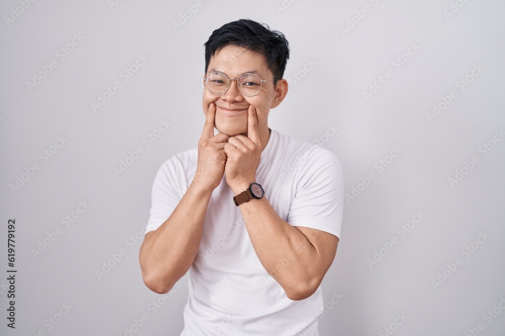 Young asian man standing over white background smiling with open mouth, fingers pointing and forcing cheerful smile Young asian man standing over white background smiling with open mouth, fingers pointing and forcing cheerful smile