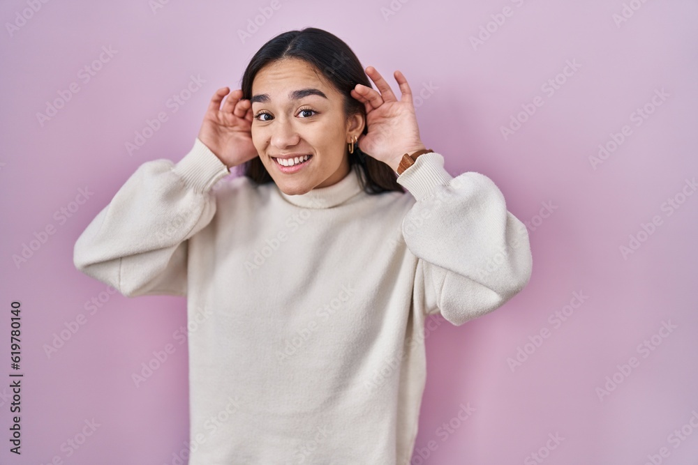 Young south asian woman standing over pink background trying to hear both hands on ear gesture, curious for gossip. hearing problem, deaf Young south asian woman standing over pink background trying to hear both hands on ear gesture, curious for gossip. hearing problem, deaf