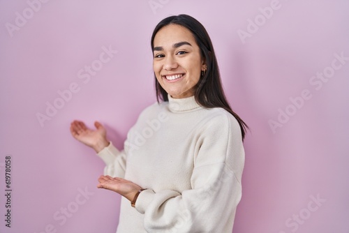 Young south asian woman standing over pink background inviting to enter smiling natural with open hand