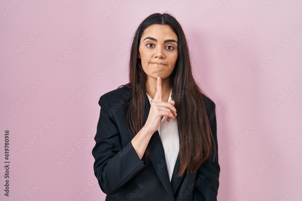 Young brunette woman wearing business style over pink background thinking concentrated about doubt with finger on chin and looking up wondering Young brunette woman wearing business style over pink background thinking concentrated about doubt with finger on chin and looking up wondering