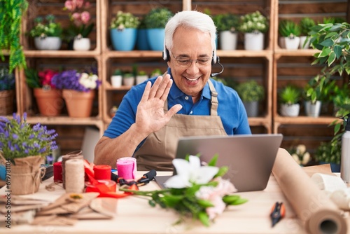 Middle age man with grey hair working at florist shop doing video call looking positive and happy standing and smiling with a confident smile showing teeth