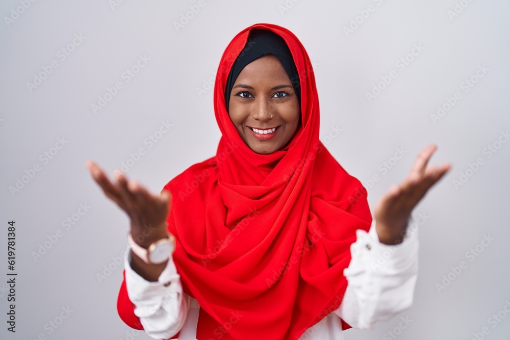 Young arab woman wearing traditional islamic hijab scarf smiling cheerful offering hands giving assistance and acceptance. Young arab woman wearing traditional islamic hijab scarf smiling cheerful offering hands giving assistance and acceptance.