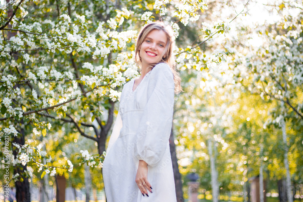 Portrait of a young woman in a white dress against the backdrop of blooming apple trees. The girl poses against the background of flowers in the spring park. Portrait of a young woman in a white dress against the backdrop of blooming apple trees. The girl poses against the background of flowers in the spring park.