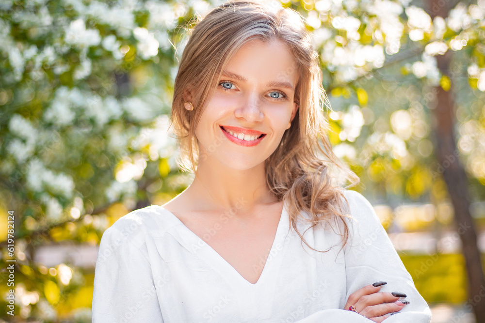 Portrait of a young woman in a white dress against the backdrop of blooming apple trees. The girl poses against the background of flowers in the spring park. Portrait of a young woman in a white dress against the backdrop of blooming apple trees. The girl poses against the background of flowers in the spring park.