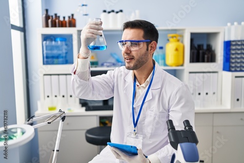 Young hispanic man scientist measuring liquid using touchpad at laboratory