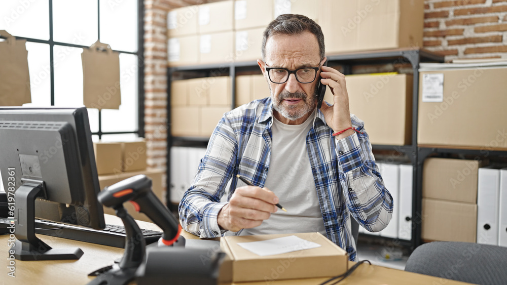 Middle age man ecommerce business worker talking on smartphone writing on package at office
