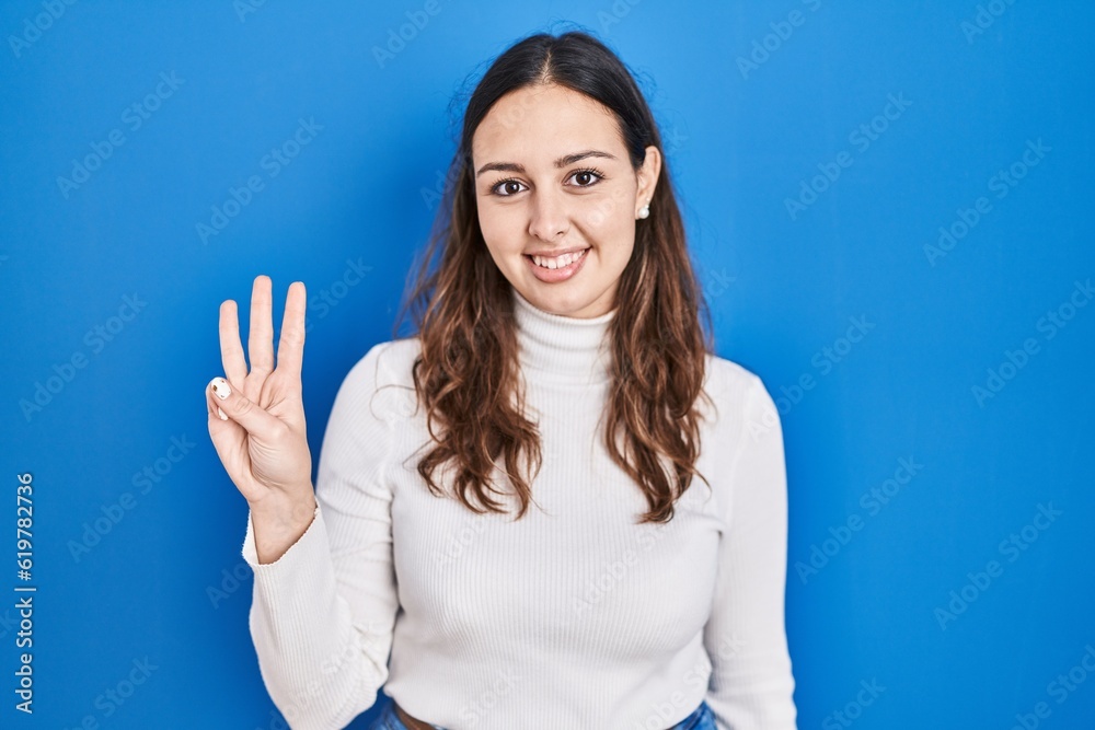 Young hispanic woman standing over blue background showing and pointing up with fingers number three while smiling confident and happy. Young hispanic woman standing over blue background showing and pointing up with fingers number three while smiling confident and happy.