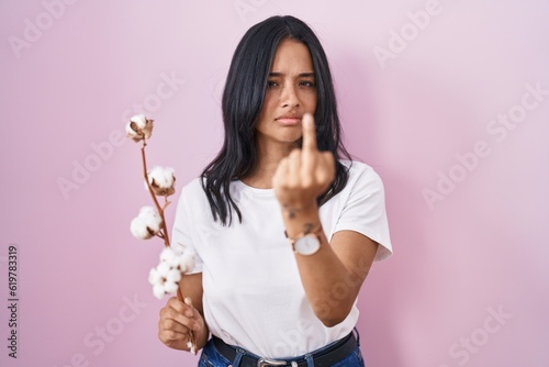 Brunette woman standing over pink background showing middle finger, impolite and rude fuck off expression