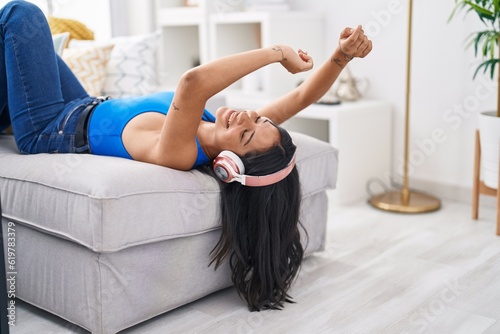 Young hispanic woman listening to music lying on sofa at home