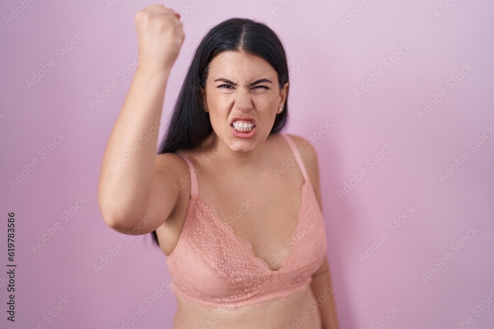 Young hispanic woman wearing pink bra angry and mad raising fist frustrated and furious while shouting with anger. rage and aggressive concept. Young hispanic woman wearing pink bra angry and mad raising fist frustrated and furious while shouting with anger. rage and aggressive concept.