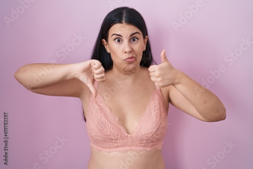 Young hispanic woman wearing pink bra doing thumbs up and down, disagreement and agreement expression. crazy conflict