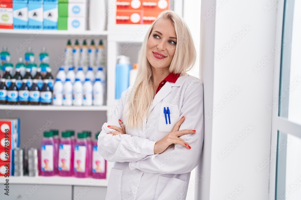 Young blonde woman pharmacist smiling confident standing with arms crossed gesture at pharmacy