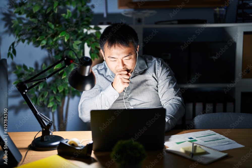Young chinese man working using computer laptop at night feeling unwell and coughing as symptom for cold or bronchitis. health care concept. Young chinese man working using computer laptop at night feeling unwell and coughing as symptom for cold or bronchitis. health care concept.