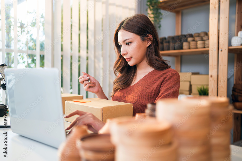 Asian beautiful woman sell vase products online live streaming at home. A young attractive girl writes the address of the customer on the parcel to send. Remote buying and purchase shopping concept. Asian beautiful woman sell vase products online live streaming at home. A young attractive girl writes the address of the customer on the parcel to send. Remote buying and purchase shopping concept.