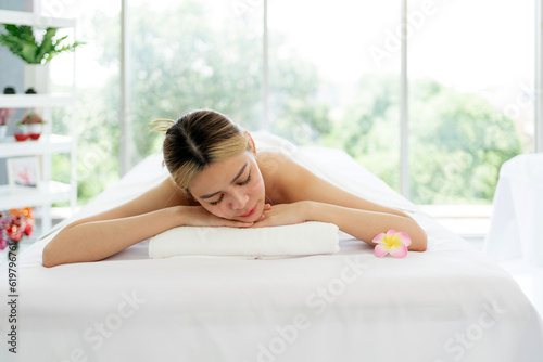 Relaxing young woman lying down and closed her eyes on massage beds at Asian luxury spa salon with white linen and wellness center, waiting for receiving massage from therapist. Spa salon concept