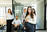 Portrait of a confident pregnant business professional in office with team at back