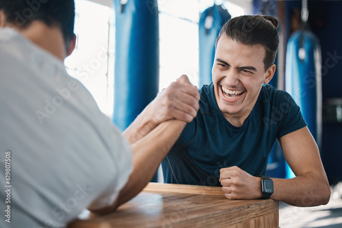 Strong, active and men arm wrestling in the gym on a table while being playful for a challenge. Rivalry, game and male people or athletes doing strength muscle battle for fun, bonding and friendship.