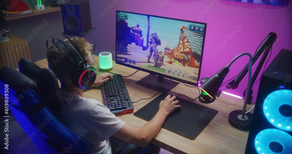 Young gamer plays third person shooter on personal computer. Schoolboy