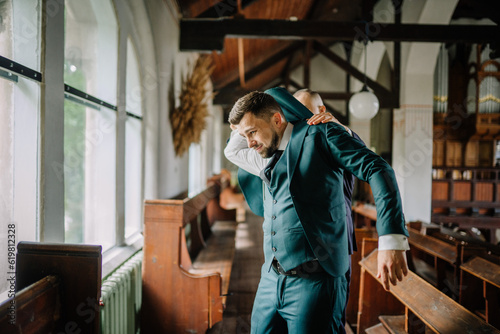 The groom carefully pulls on a green jacket as he prepares for the upcoming wedding ceremony, ensuring every detail of his attire is immaculate