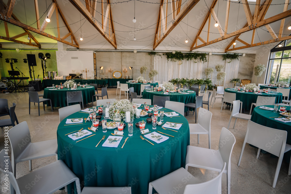 Fototapeta premium The venue is decorated for a wedding with round tables and green tablecloths, it looks unique and beautiful