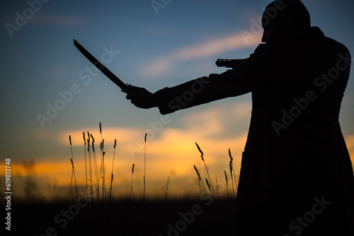 Silhouette of a demon and vampire hunter with a dramatic sky in the background. A man with a katana and a revolver. Fantasy and halloween concept